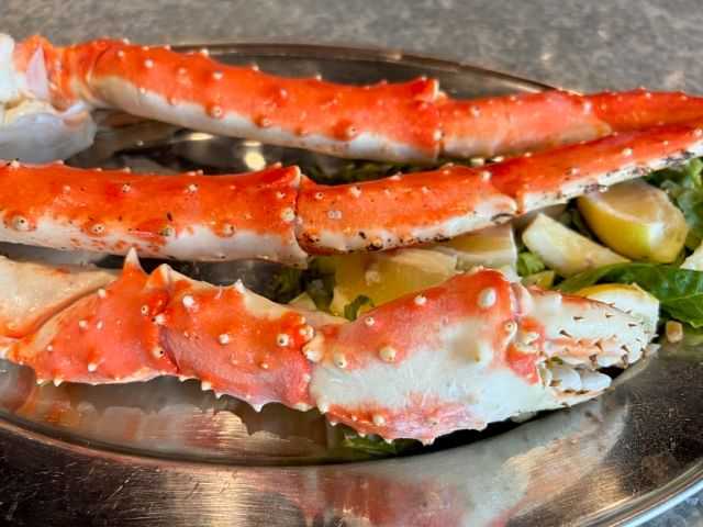 King crab legs on a metal plate with lemon wedges and greens.