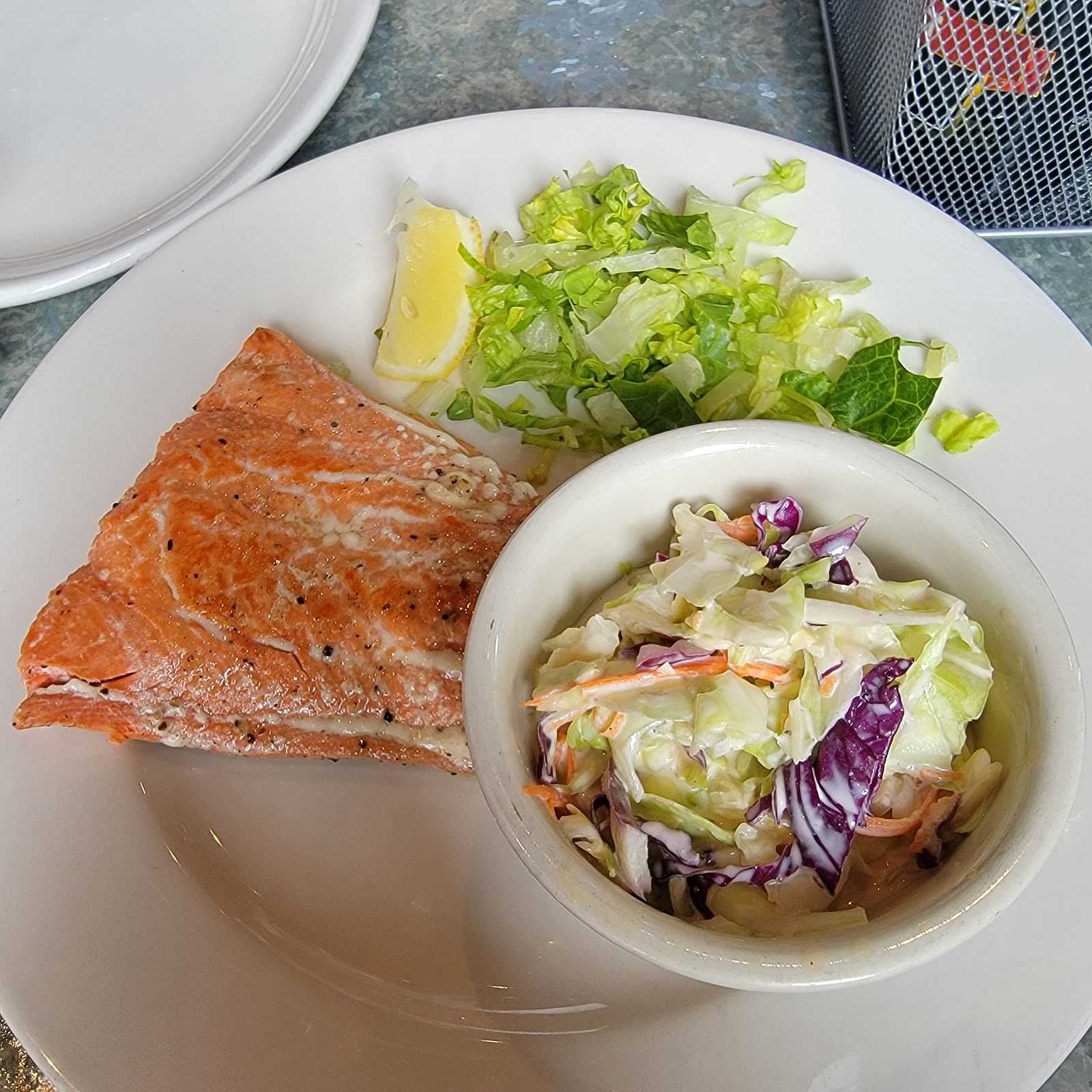 Grilled salmon with side of coleslaw and fresh salad on a plate.