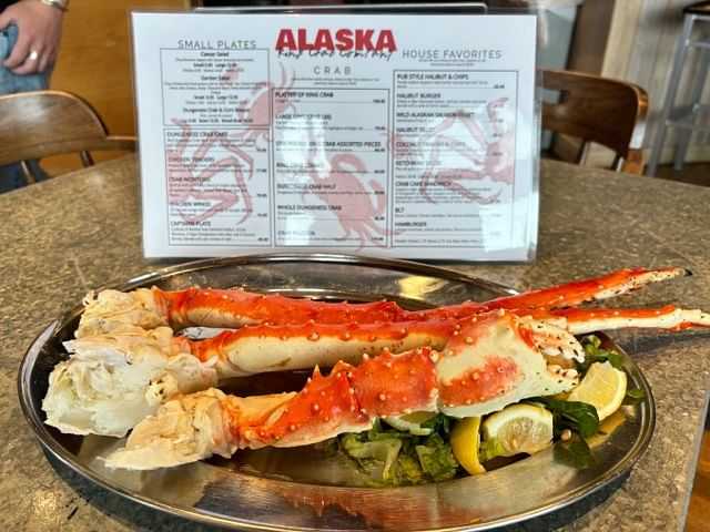 Plate with Alaskan king crab legs on greens and lemon slices, menu in the background.