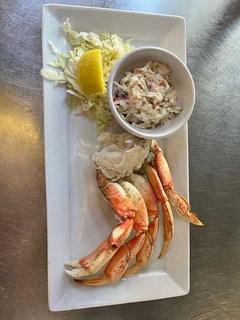 Plate of crab legs with a slice of lemon, coleslaw, and shredded cabbage on a white rectangular dish.