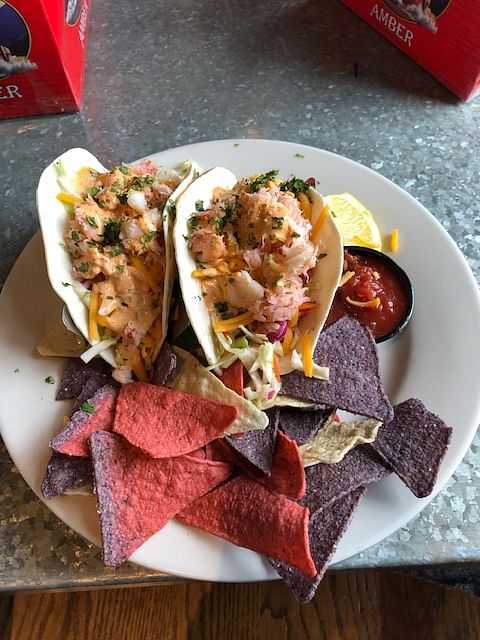 Two shrimp tacos with slaw and a side of colorful tortilla chips.