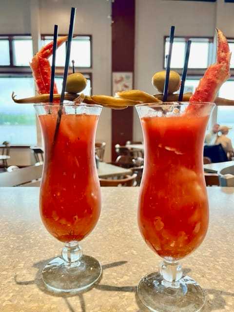 Two Bloody Mary cocktails garnished with crab legs, skewered olives, and pickled vegetables.