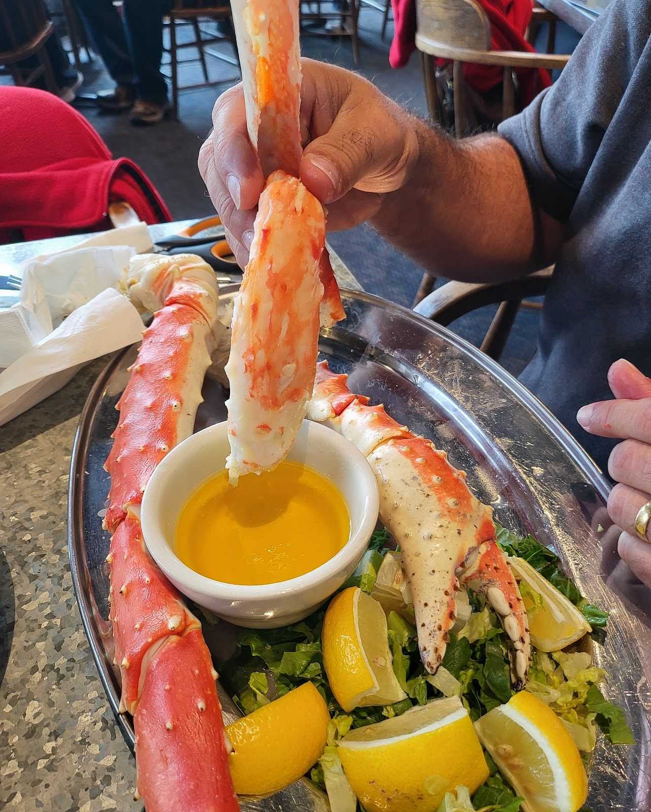 Person dipping a large crab leg into butter with more crab legs on a plate.