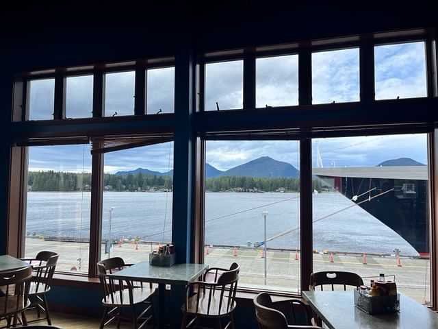 View of mountains and a harbor through large windows in a cozy waterfront restaurant.