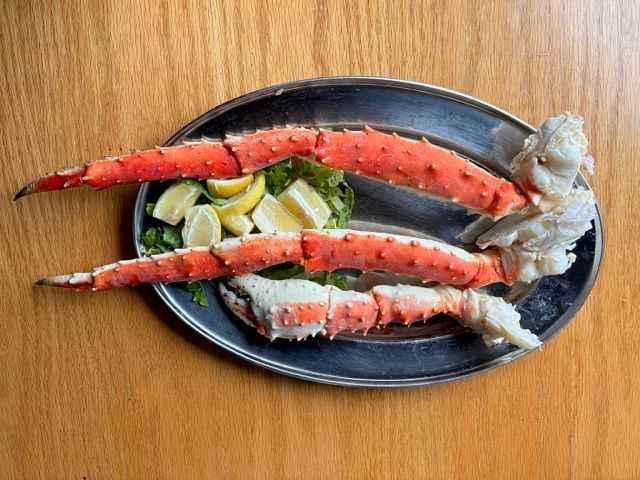 Plate of crab legs with lemon wedges and greens on a wooden table.