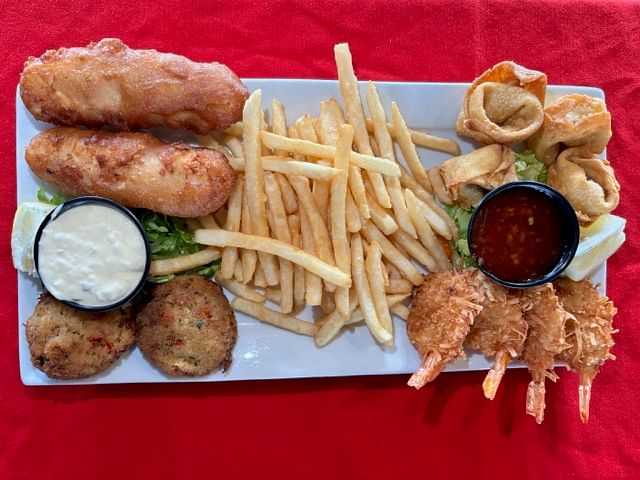 A platter with fish, fries, hush puppies, fried shrimp, and dipping sauces on a red tablecloth.