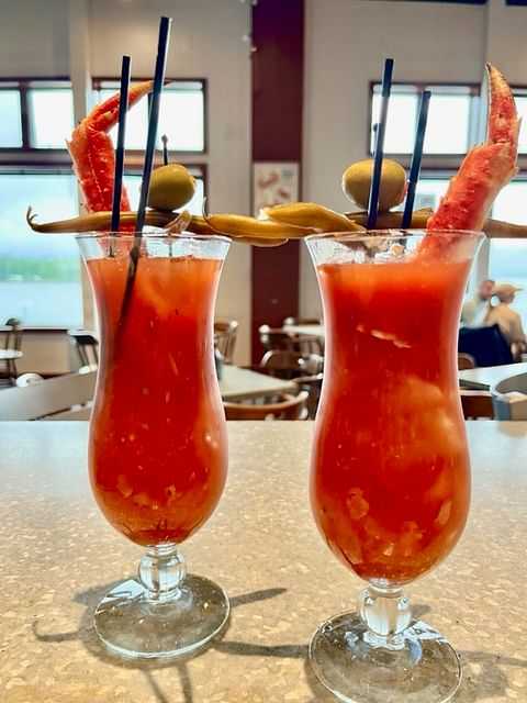 Two Bloody Mary cocktails garnished with crab legs, skewered olives, and pickled vegetables.