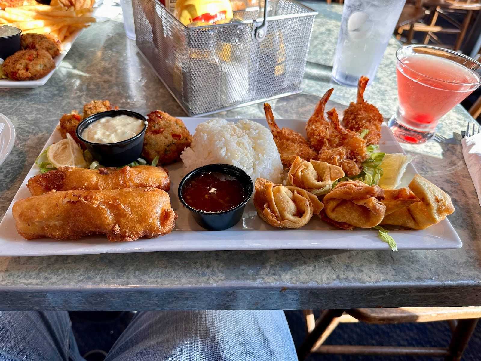 A platter of various fried appetizers with dipping sauces and rice.